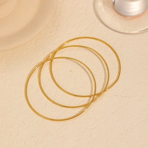 Drei minimalistische 18k vergoldete Titanstahlarmreifen auf strukturiertem Hintergrund