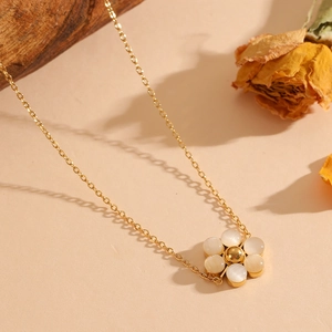 Detail of a gold floral necklace with white cat-eye stone petals on a beige natural background