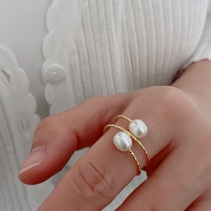 Detail of twisted gold ring band with two lustrous freshwater pearls on finger