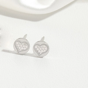 Detailed macro view of silver heart studs with textured relief on white silk background