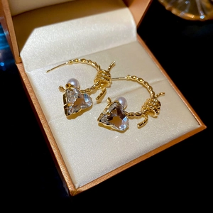 Detail of gold C-shape pearl earrings with heart-shaped crystal in a velvet box