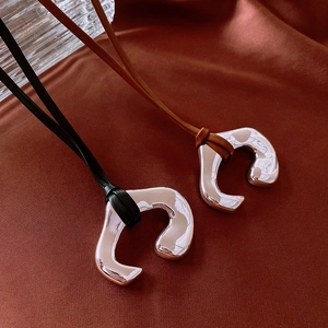 Close-up of irregular silver horseshoe pendant on faux leather cord over silk fabric