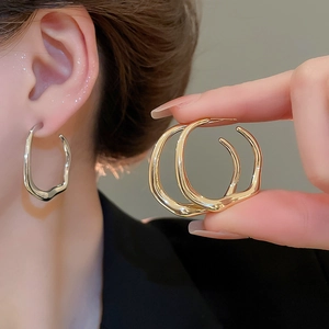 Detail of twisted irregular circular gold and silver earrings on model ear and hand