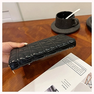 Close-up of black quilted leather long wallet with zipper detail held by hand on a desk