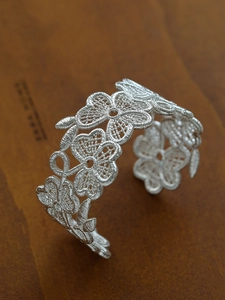 Macro shot of silver lace open bangle with intricate floral cut-out textures and metallic glow
