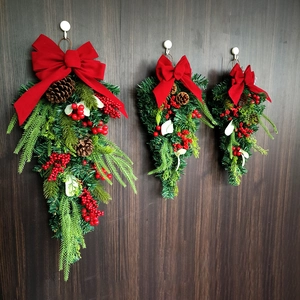 Detail of Christmas teardrop swag with red bows, pine cones, and red berries on wood