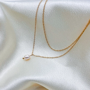 Detail shot of a white pearl pendant on a gold metal chain against silk fabric