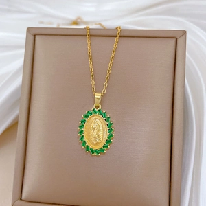 Golden oval pendant necklace with religious figure and emerald green zircons on a display