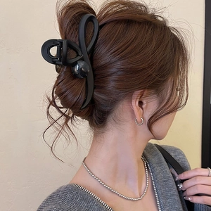 Detail of matte black cross hair claw clip with pearl on model's elegant updo