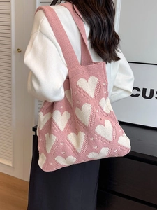 Chic pink knitted tote bag with white heart patterns shown on a model's shoulder