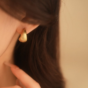 Close-up of model wearing gold waterdrop hoop earrings with a matte brushed finish