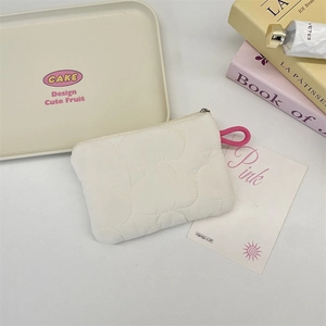 Close-up of white quilted cloud coin purse with pink lanyard handle on white decorative tray