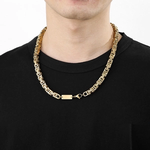 Détail d'un collier homme à maillons carrés dorés porté sur un t-shirt noir élégant