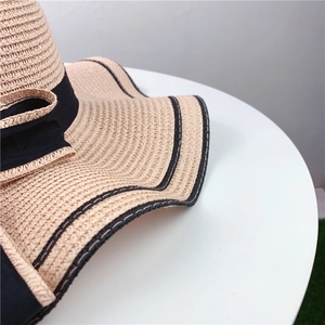 Close-up of beige woven straw hat featuring black ribbon bow and elegant trim details
