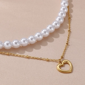 Detail of double-layer pearl necklace featuring a golden chain and open heart pendant