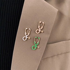 Three stethoscope brooches in gold, silver, and green on a khaki blazer lapel