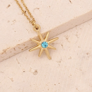 Detail of a gold sunburst pendant with a blue gemstone on a beige stone surface