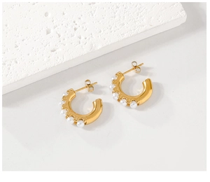 Macro detail of C-shaped gold-plated stainless steel earrings with white faux pearls