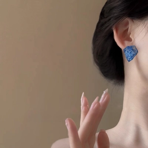 Blue irregular resin earrings with glitter on a female model against a beige backdrop