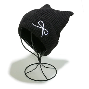 Detail of black knit beanie with cat ears and white bow embroidery on a metal display stand