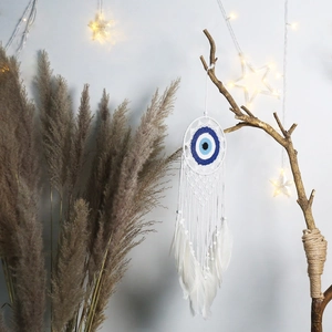 Detail eines handgefertigten Evil Eye Traumfängers mit weißen Federn und Perlen an Wand