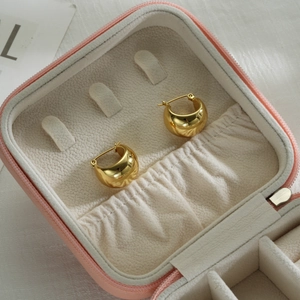 Detailed macro view of chunky gold hollow oval hoop earrings on a soft pink jewelry box