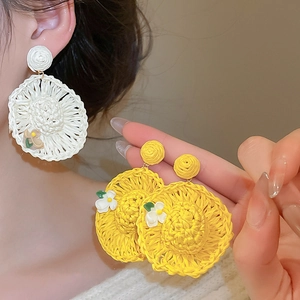Detailed macro view of woven straw hat earrings with 3D floral accents and summer vibes