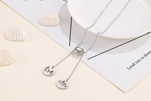 Detail of silver heart lariat necklace with family silhouette charms on a ceramic plate