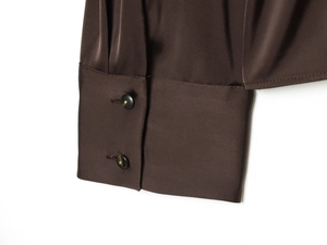 Détail du poignet d'une chemise en satin marron avec deux boutons en résine et texture