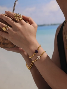 Detail of 18k gold plated beaded bracelet with natural agate and a cross charm by the sea