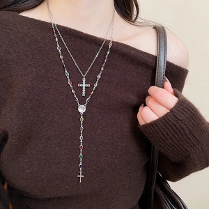 Detail of silver layered cross necklace with colorful beads on dark sweater