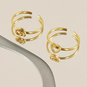 Golden stainless steel rings with flower and heart designs on a mirror surface
