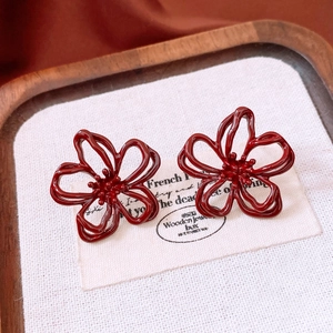 Detail view of red floral enamel earrings on a wooden display tray with white fabric