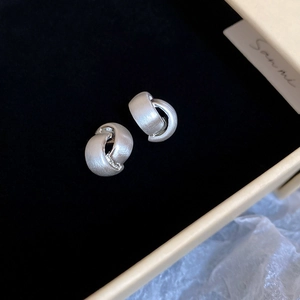 Macro shot of brushed silver irregular C-shape knot earrings on a black velvet background
