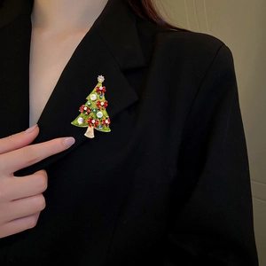 Close-up of a green enamel Christmas tree brooch with colorful rhinestones on a black suit