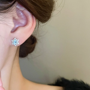 Close-up of a silver snowflake earring with a light blue zircon on a model ear