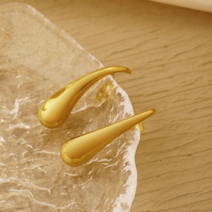 Detail of large golden teardrop earrings with a polished mirror finish on glass tray