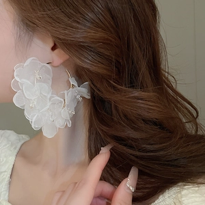 Close-up of elegant large white lace flower earrings with beads on gold metal hoops