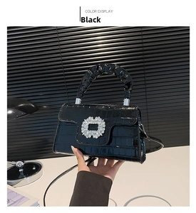 Détail d'un sac à main noir texture crocodile avec boucle fleurie en strass brillants