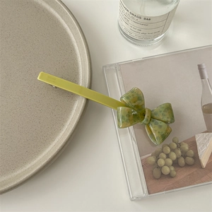 Flat lay of a yellow acetate hair clip with a green bow on a minimalist beige ceramic plate