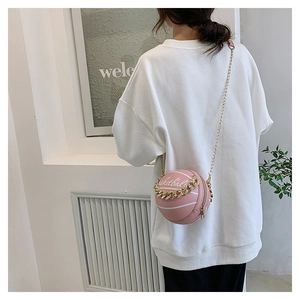 Pink basketball shaped crossbody bag with gold chain strap shown on model outdoors