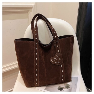 Detail of dark brown suede tote bag with silver rivets and heart charm on a white chair