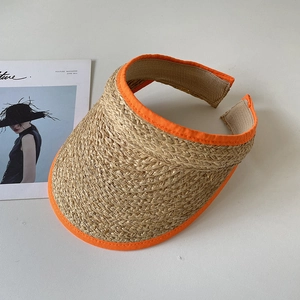 Détail d'une visière en raphia naturel avec bordure en tissu orange vif sur fond beige