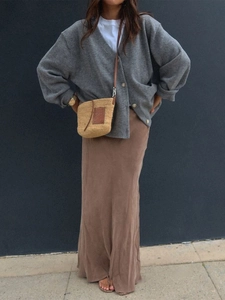 Detail of grey knitted cardigan paired with a brown maxi skirt and straw crossbody bag