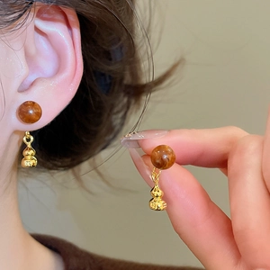 Détail de boucles d'oreilles en perle ambrée avec pendentif gourde dorée rétro