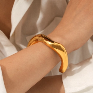 Close-up of golden chunky irregular cuff bracelet styled on a wrist with a white shirt