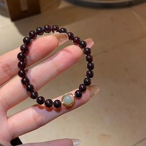 Close-up of garnet beaded bracelet with a green jade accent in a golden ring charm