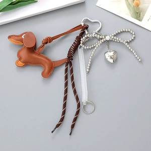 Brown leather dachshund keychain with striped cord and silver bow charm on a grey background