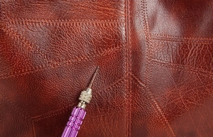Macro view of brown lychee-textured leather with precise stitching on a bucket bag