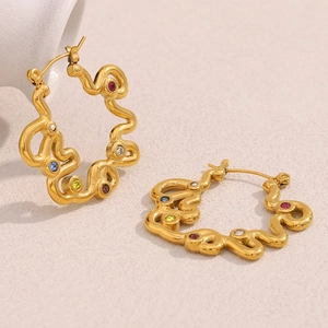 Irregular wave-shaped gold earrings with colorful gemstones on a textured background